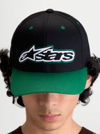 Alpinestars Gorra Retro Snapback, gorra de sarga de algodón inspirada en el motorsport, negra y verde, vista frontal en modelo con logotipo Astars y pespunte verde, visera curva y corona estructurada