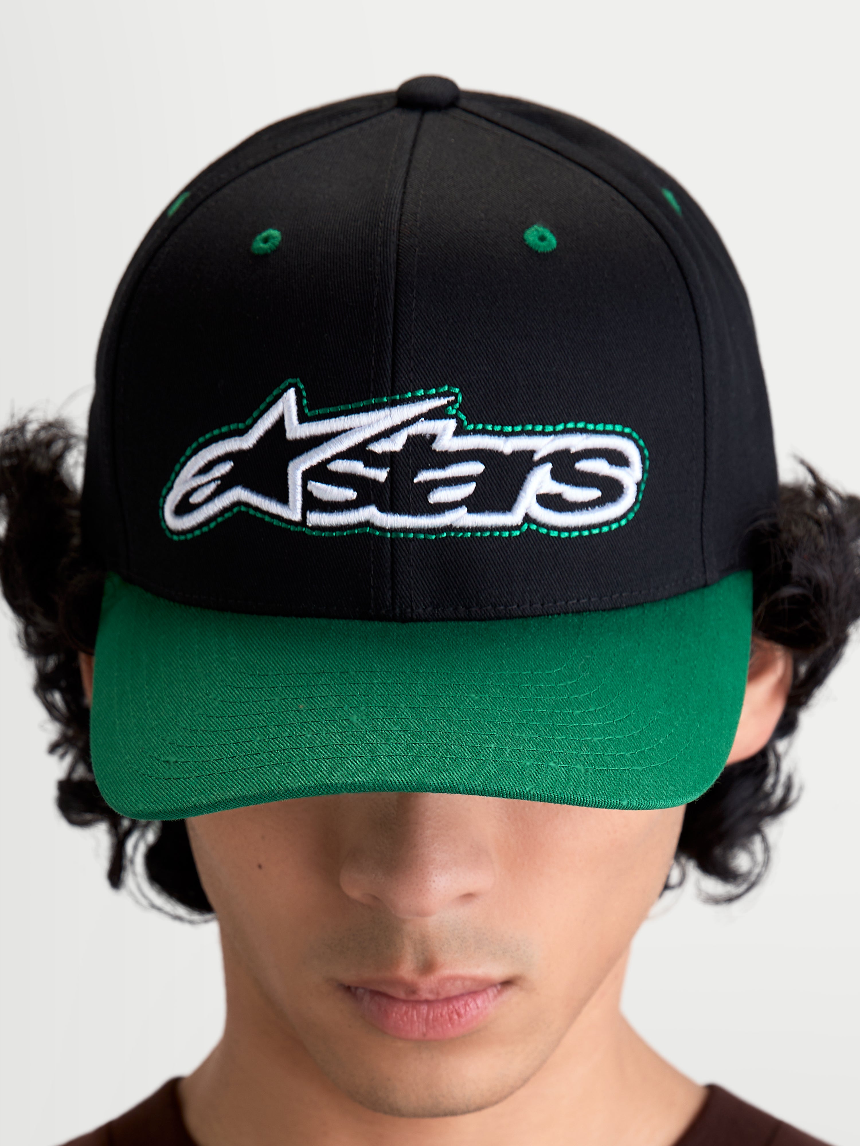 Alpinestars Gorra Retro Snapback, gorra de sarga de algodón inspirada en el motorsport, negra y verde, vista frontal en modelo con logotipo Astars y pespunte verde, visera curva y corona estructurada
