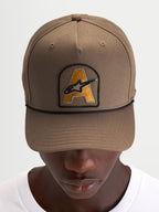 Gorra Alpinestars Acme Snapback, gorra de sportswear con visera curva, marrón nuez con parche bordado del logotipo Astars en el frontal y ribete de cuerda negro, vista frontal en modelo