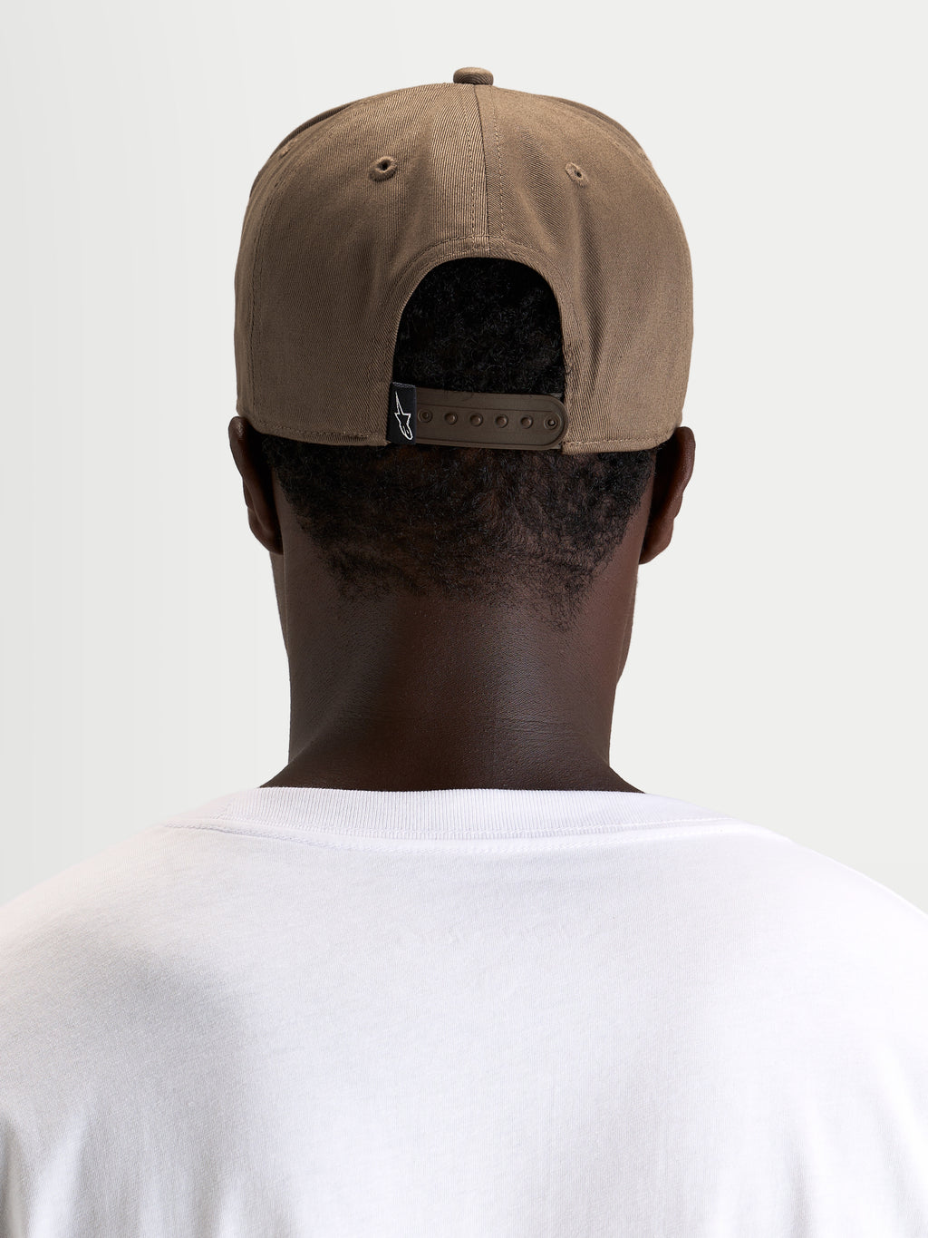 Gorra Acme Snapback Alpinestars, gorra casual sportswear, marrón nogal, vista trasera en modelo mostrando el cierre snapback ajustable y la etiqueta trasera de la marca
