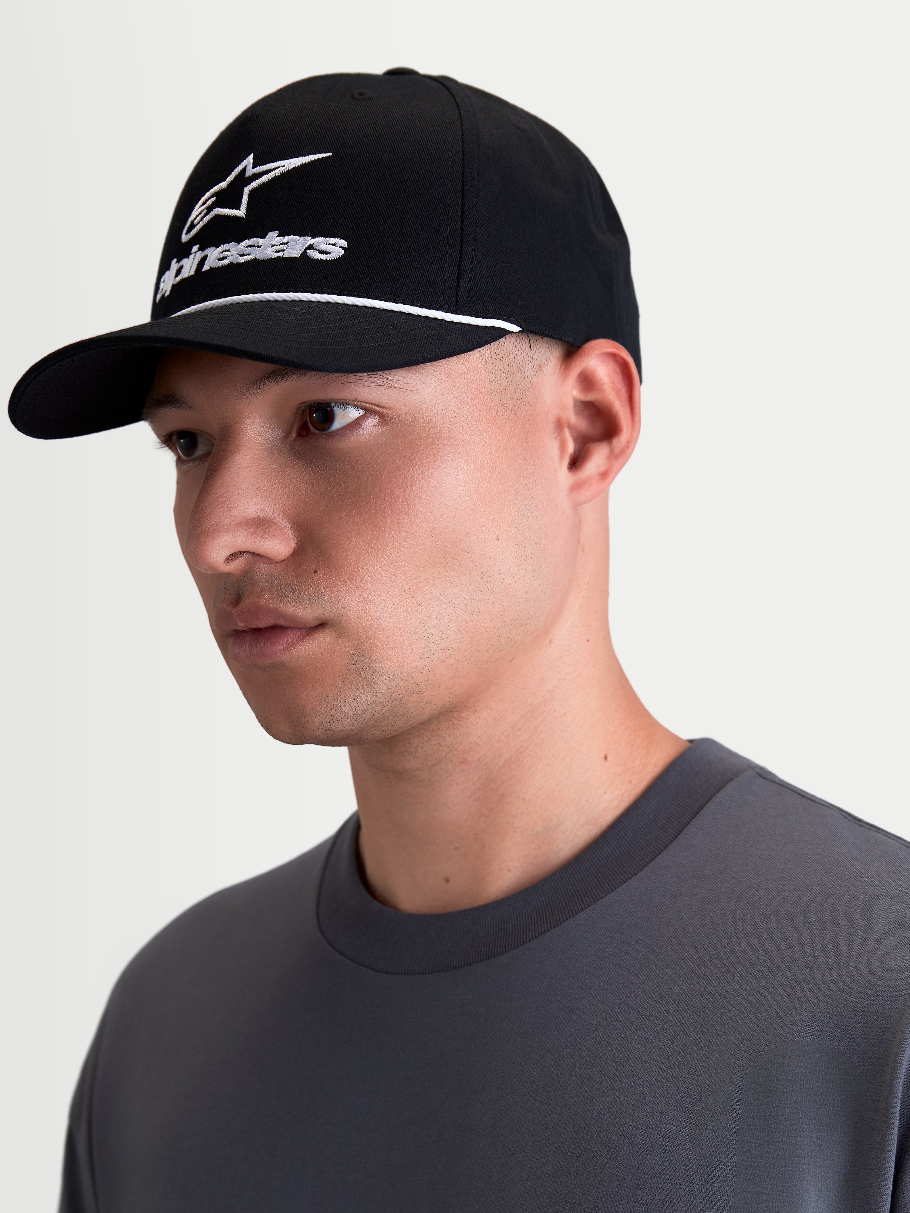 Alpinestars Gorra Combo Logo Snapback, gorra de ropa deportiva estilo lifestyle, negra y blanca, con visera curva, corona estructurada, bordado blanco y detalle de cordón, mostrada en un modelo de perfil.