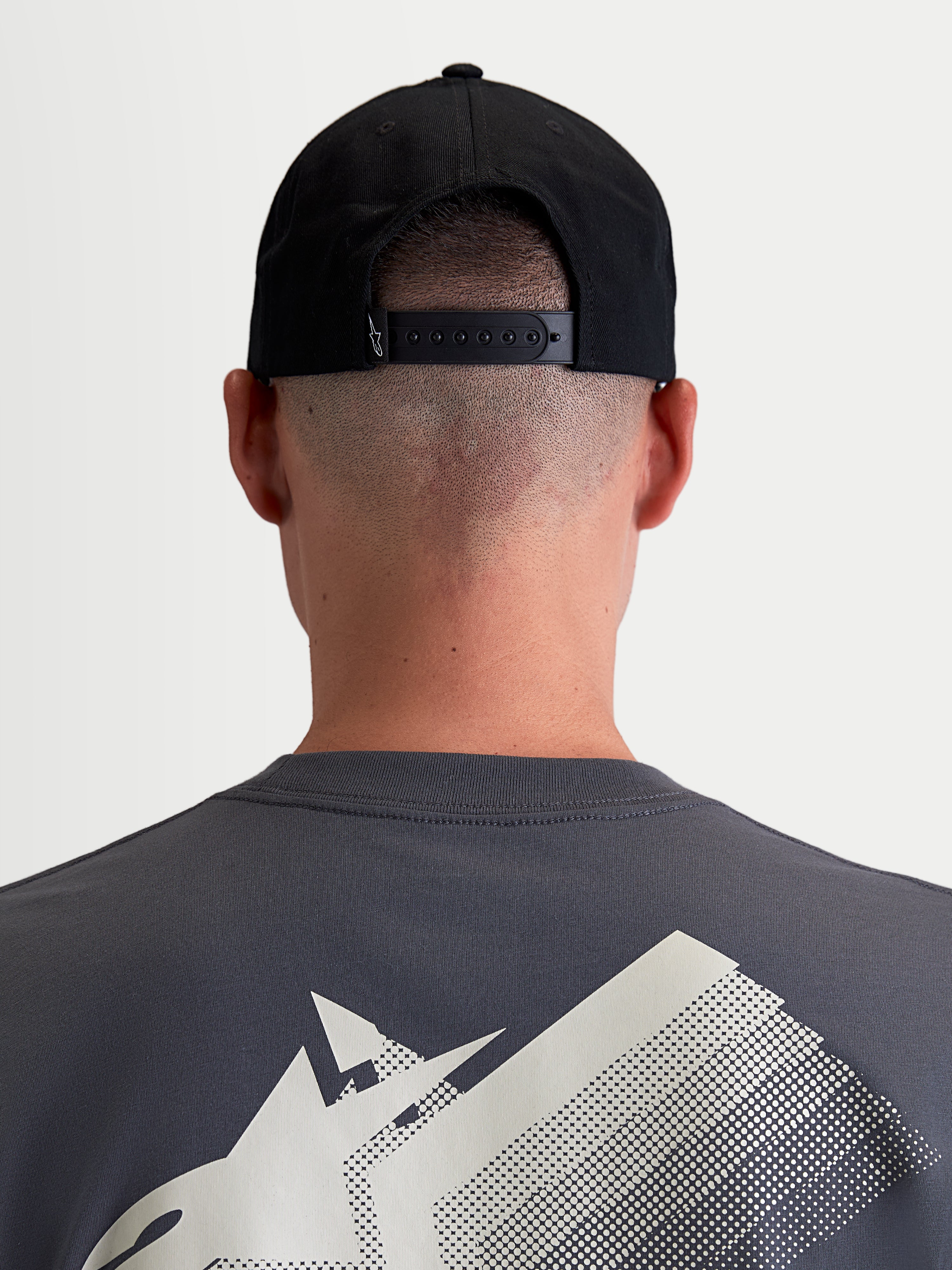 Alpinestars Gorra Combo Logo Snapback, gorra de estilo motorsport para hombre y mujer, negra, confeccionada en sarga de algodón duradera, vista trasera en modelo que muestra el cierre snapback ajustable y un pequeño logotipo blanco.