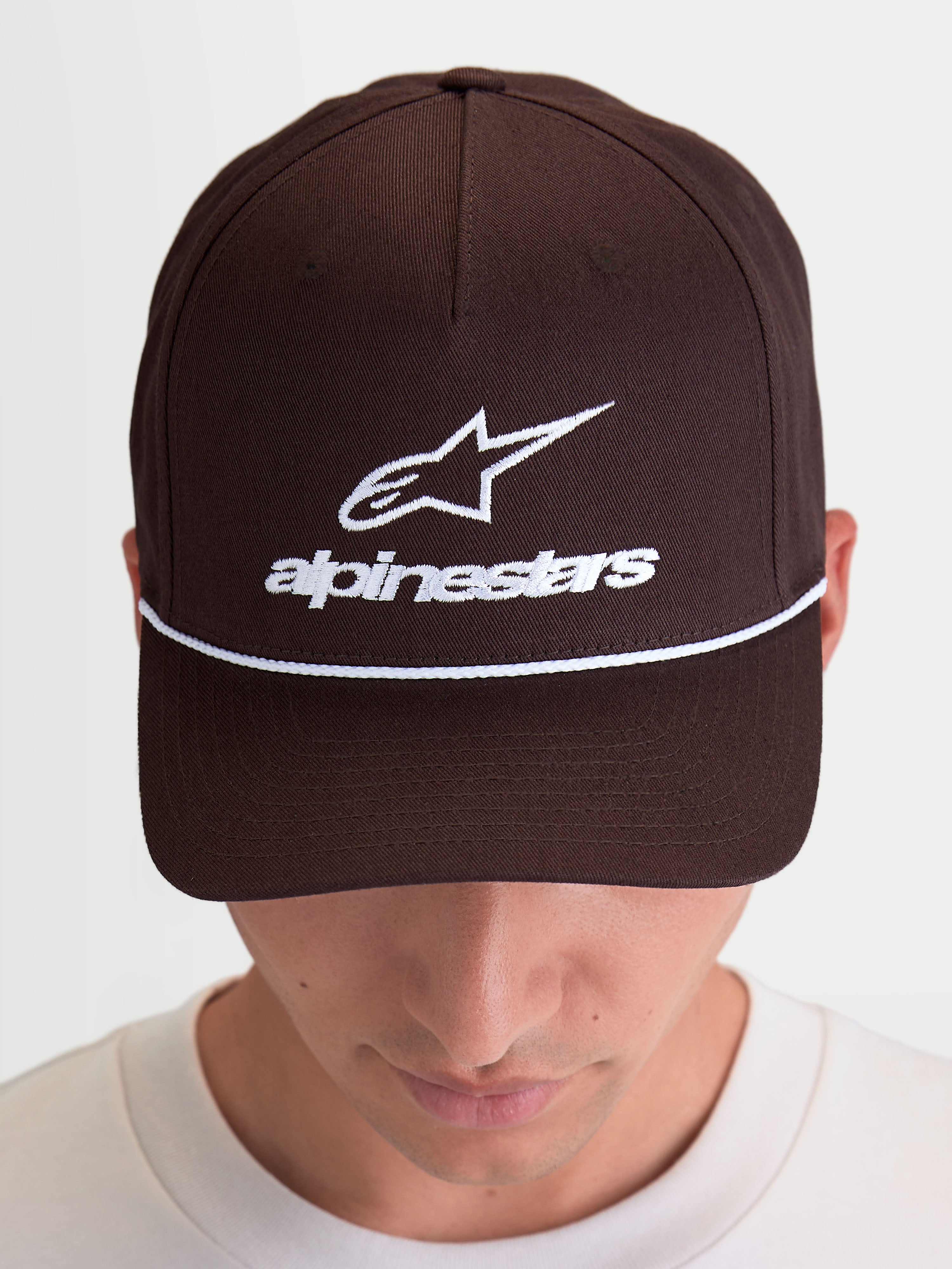 Alpinestars Gorra Combo Logo Snapback, gorra de estilo sportswear marrón con bordado blanco, visera curva y corona estructurada, logotipo Astars y marca denominativa en el frontal, construcción de sarga de algodón, mostrada en modelo.