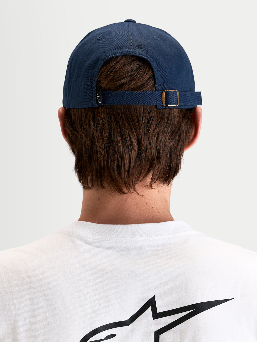 Gorra Dylan Dad Alpinestars, gorra deportiva informal en azul marino, vista trasera que muestra el cierre ajustable con hebilla metálica y pequeña etiqueta con el logo Astars llevada por un modelo