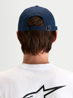 Gorra Dylan Dad Alpinestars, gorra deportiva informal en azul marino, vista trasera que muestra el cierre ajustable con hebilla metálica y pequeña etiqueta con el logo Astars llevada por un modelo