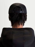 Alpinestars Gorra Gravel, gorra de estilo trucker unisex, color negro, vista trasera en modelo mostrando la malla de poliéster transpirable y el cierre ajustable a presión.