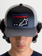 Alpinestars Gorra Gravel, gorra de estilo trucker para ropa deportiva, gris oscuro y negra, visera curva, parche frontal tejido con texto Racing Ahead y logotipo Astars, vista frontal en modelo
