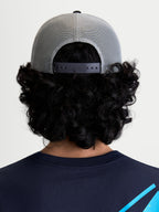 Alpinestars Gorra Gravel, gorra de estilo trucker para ropa deportiva, vista trasera en modelo que muestra la parte trasera de malla transpirable y el cierre ajustable a presión, gris y negra.
