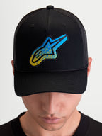 Alpinestars Gorra Meteorite, gorra de estilo sportswear con corona estructurada y visera curva, negra con logotipo Astars texturizado en azul y amarillo, panel trasero de malla, puesta por un modelo