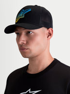 Alpinestars Gorra Meteorite, gorra de estilo trucker para hombre, negra con panel trasero de malla transpirable, visera curva y corona estructurada. Presenta un parche tejido con el logotipo Astars de textura gravel en azul y amarillo, estilo casual sportswear mostrado en modelo