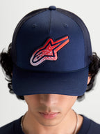 Alpinestars Gorra Meteorite, gorra de estilo trucker azul marino con parche del logotipo Astars en rojo y blanco con textura gravel, corona estructurada y visera curva, vista frontal en modelo