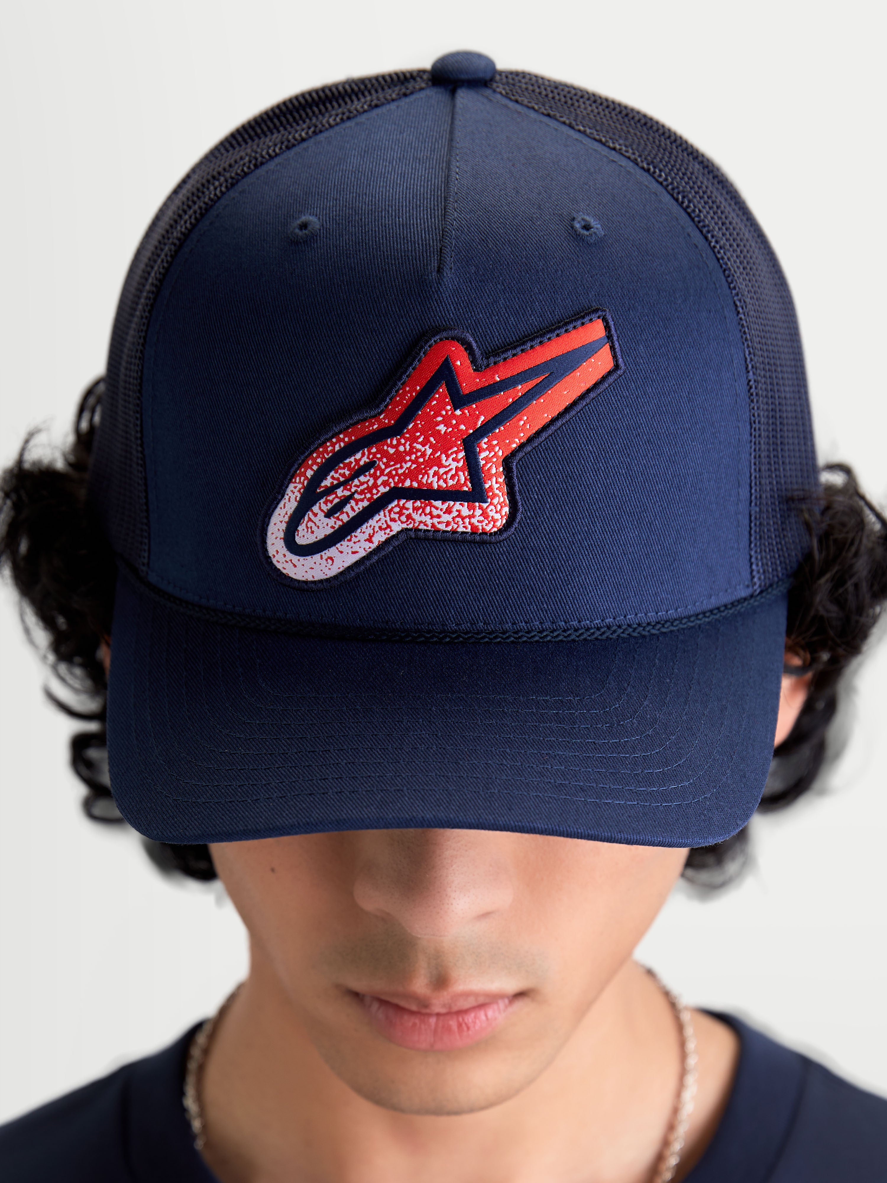 Alpinestars Gorra Meteorite, gorra de estilo trucker azul marino con parche del logotipo Astars en rojo y blanco con textura gravel, corona estructurada y visera curva, vista frontal en modelo