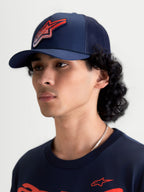 Alpinestars Gorra Meteorite, gorra de estilo trucker, azul marino y roja, visera curva y corona estructurada, panel trasero de malla, logotipo Astars con textura gravel, ropa deportiva, vista en modelo