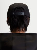Alpinestars gorra Label Snapback, gorra sportswear unisex, negra, vista trasera en modelo mostrando el cierre snapback ajustable con pequeño logotipo blanco, construcción de sarga de algodón estructurada