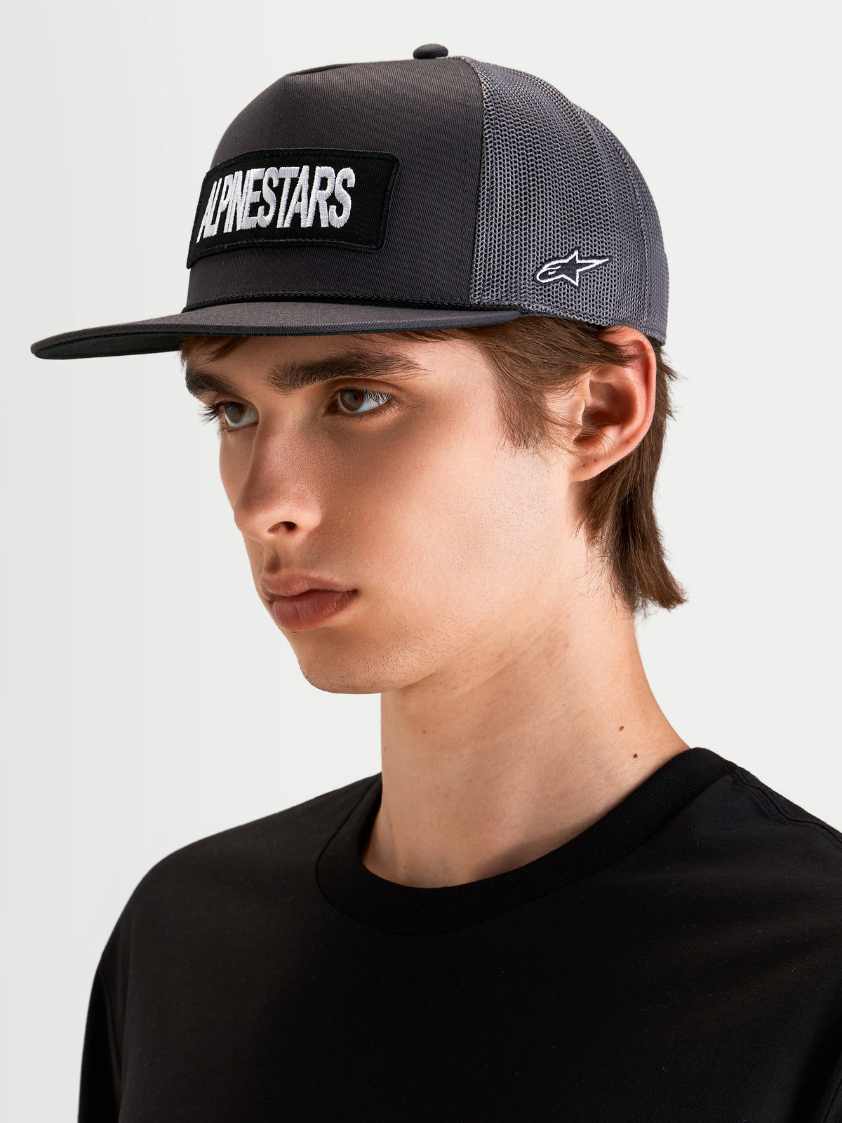 Gorra Ten Alpinestars, gorra trucker sportswear con visera plana en gris oscuro, vista en modelo con parche bordado frontal y logotipo lateral Astars