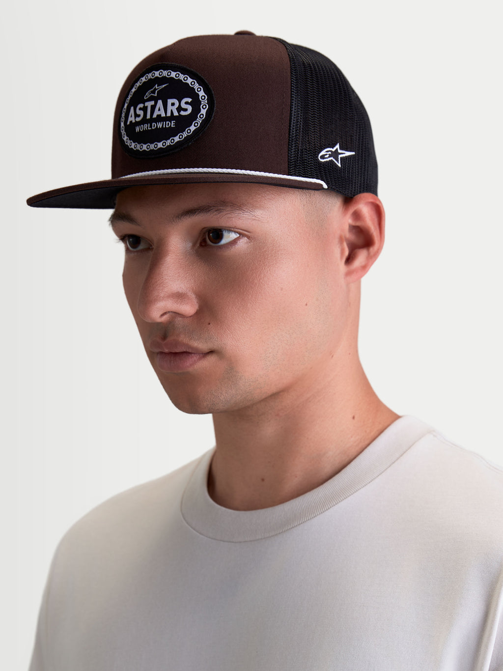 Alpinestars Hotlink Trucker Hat on Model, Brown and Black Lifestyle Sportswear Cap with Flat Bill, Structured Twill Crown, and Front Astars Logo Woven Patch with Bike Chain Border