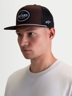 Alpinestars Hotlink Trucker Hat on Model, Brown and Black Lifestyle Sportswear Cap with Flat Bill, Structured Twill Crown, and Front Astars Logo Woven Patch with Bike Chain Border