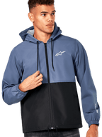 Male model wearing Alpinestars Speeder Windbreaker Jacket, Slate Blue and Black color-blocked design, hooded with black drawcords, white logo on chest, casual motorsport-inspired windbreaker