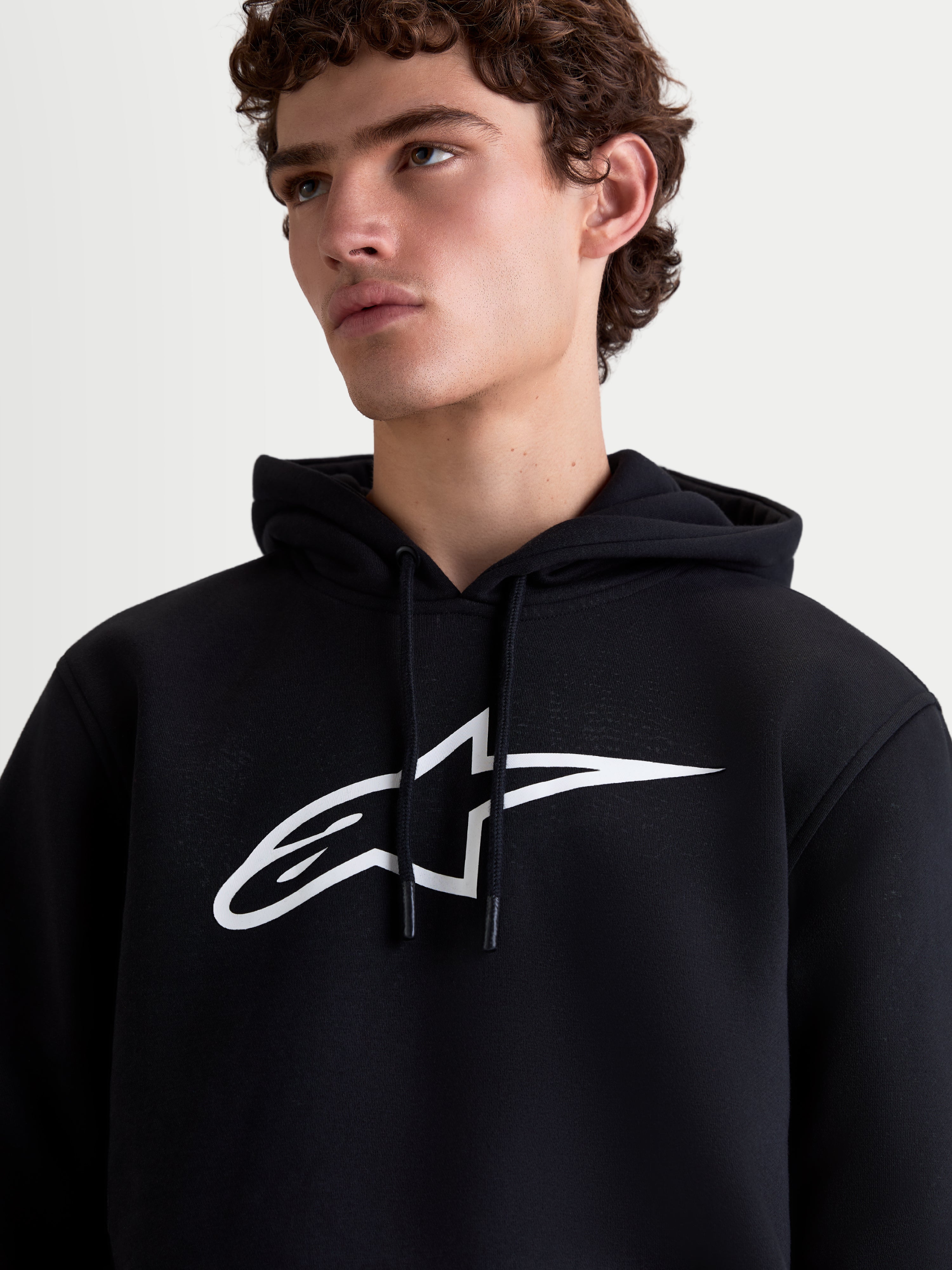 Alpinestars Ageless V3, sudadera con capucha para hombre, negra y blanca, ropa deportiva de forro polar, logotipo bordado blanco en el pecho, cordones con puntas engomadas, vista de cerca en modelo.