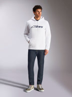 Alpinestars Blaze V3 Hoodie, white casual streetwear hoodie with navy Alpinestars logo on the chest, worn by a model with dark blue jeans and tan sneakers, featuring a drawstring hood and front pouch pocket