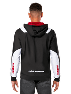 Alpinestars Sessions V3 Hoodie, vista trasera, negra con paneles blancos en las mangas y forro rojo en la capucha, con logotipo blanco en la espalda y marca roja en las mangas, ropa urbana casual inspirada en el automovilismo