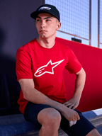 Gorra Alpinestars Profile en color negro, foto de estilo de vida de un hombre usando la gorra de visera curva con una camiseta roja con el logotipo de Alpinestars en blanco, estilo streetwear casual inspirado en el motor