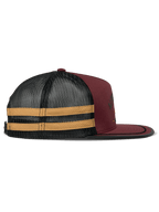 Gorra Trucker Alpinestars Backline, color ladrillo, negro y mostaza, vista de perfil lateral, frontal de sarga rojo oscuro con malla trasera negra y franjas laterales amarillas, visera plana con ribete de sutache negro, accesorio casual inspirado en el automovilismo
