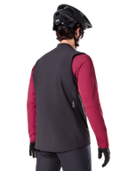 Chaleco térmico Alpinestars A-Dura, negro, vista trasera, puesto sobre un jersey granate de manga larga con casco y guantes negros de MTB, equipamiento de ciclismo ligero y aislado para rutas todoterreno