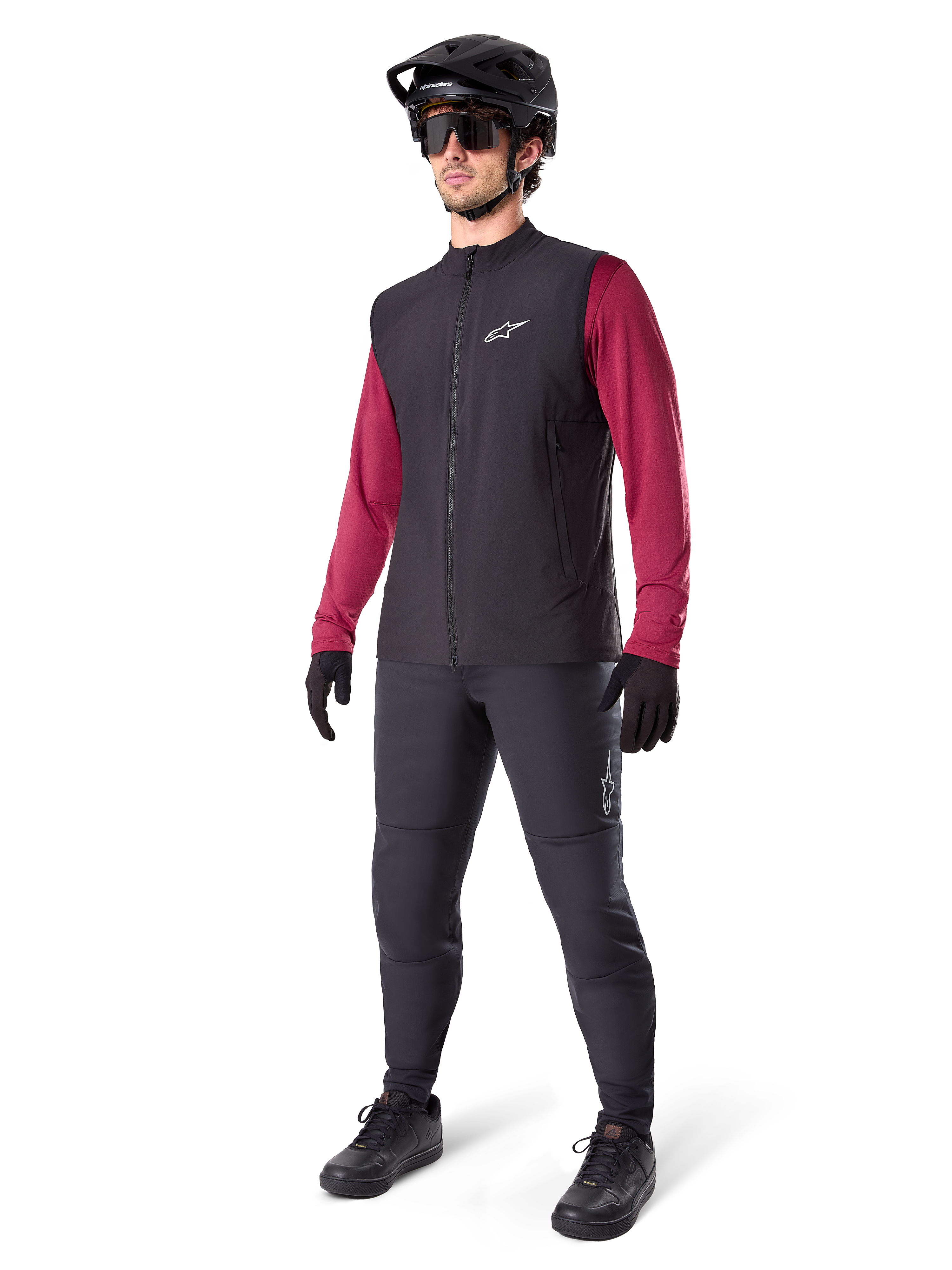 Chaleco Térmico Alpinestars A-Dura, chaleco de ciclismo negro, usado por un ciclista sobre un jersey de manga larga granate y pantalones negros, con casco de MTB y guantes negros, diseñado para ciclismo de montaña en climas fríos