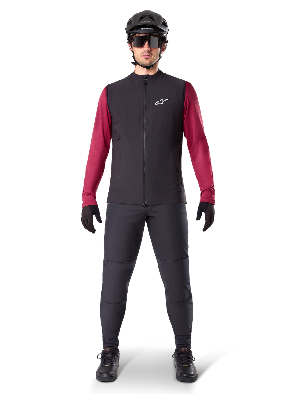 Alpinestars Chaleco Térmico A-Dura, chaleco de ciclismo negro sobre un jersey granate de manga larga, combinado con pantalones de MTB gris oscuro, casco y gafas de sol negras, ropa técnica de bicicleta de montaña para climas fríos