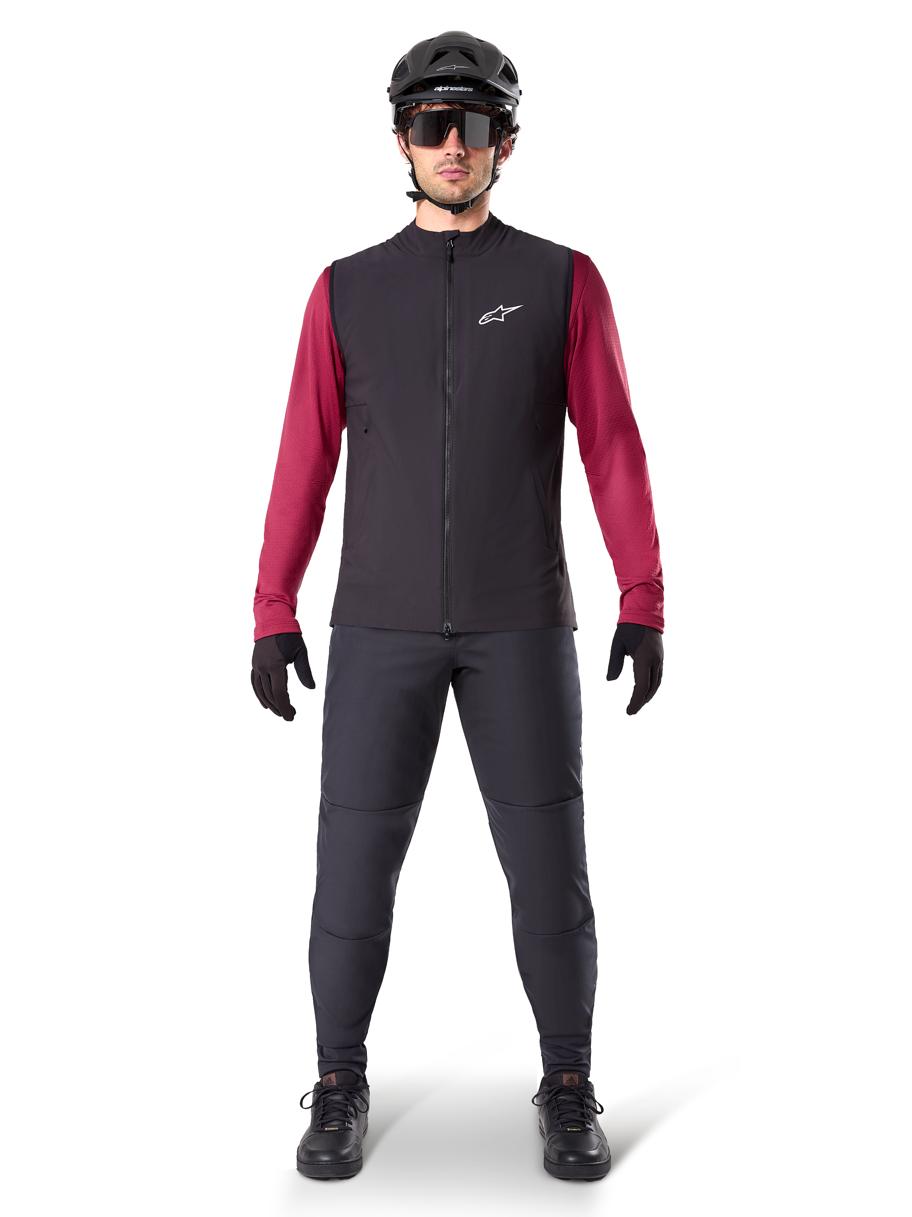 Alpinestars Chaleco Térmico A-Dura, chaleco de ciclismo negro sobre un jersey granate de manga larga, combinado con pantalones de MTB gris oscuro, casco y gafas de sol negras, ropa técnica de bicicleta de montaña para climas fríos