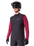 Alpinestars A-Dura Thermal Vest, chaleco térmico de ciclismo negro, usado sobre una camiseta de manga larga granate, con logotipo blanco en el pecho, combinado con casco de MTB negro y gafas de sol, capa de rendimiento con aislamiento para ciclismo de montaña