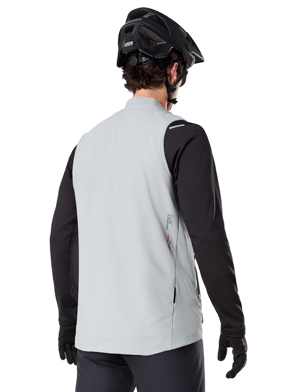 Chaleco térmico Alpinestars A-Dura, Gris Titanio, vista posterior del modelo con jersey de manga larga negro y casco de MTB, diseño minimalista con logo de estrella roja en la espalda, chaleco de ciclismo ligero y aislado para ciclismo de montaña