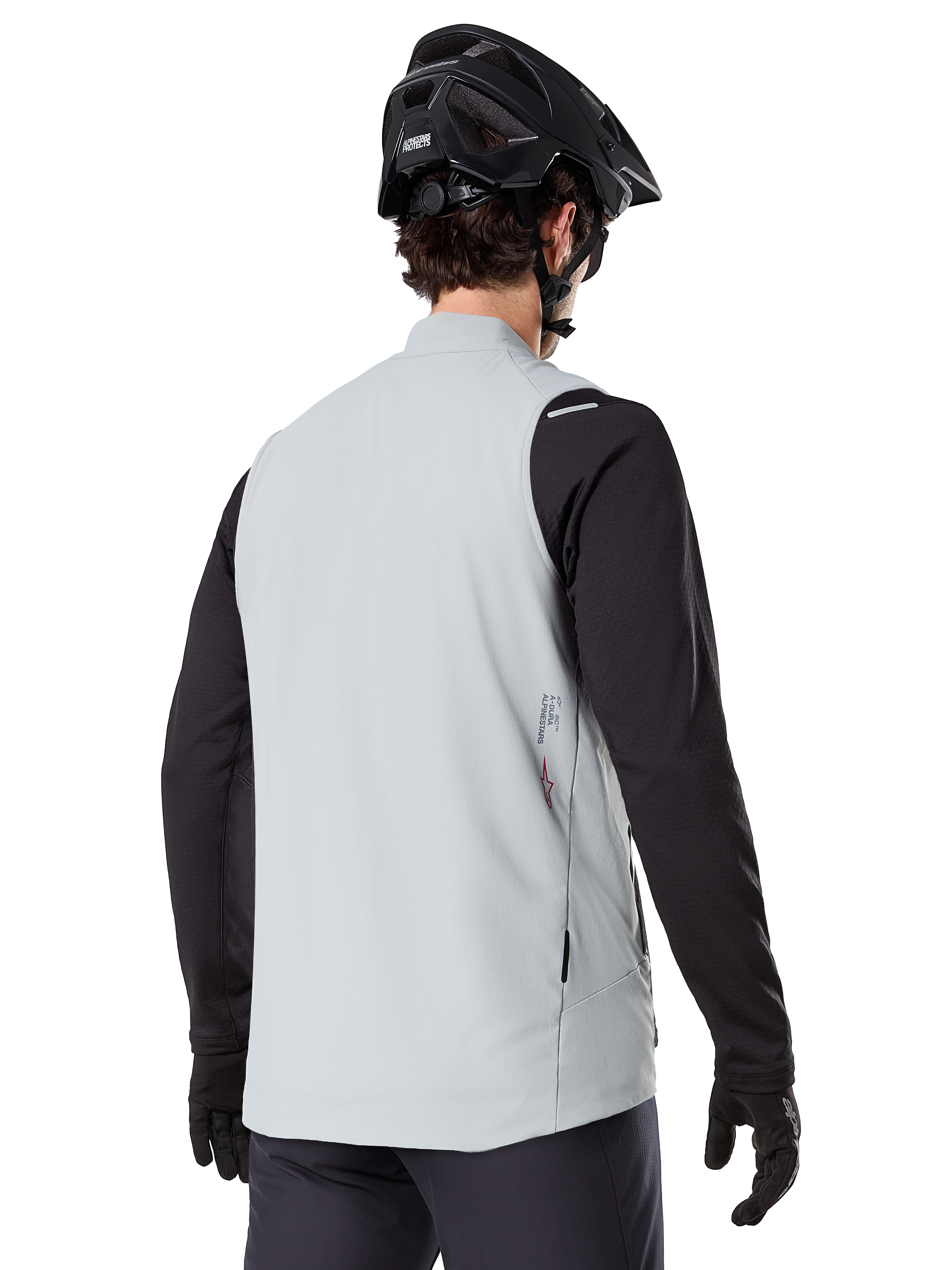 Chaleco térmico Alpinestars A-Dura, Gris Titanio, vista posterior del modelo con jersey de manga larga negro y casco de MTB, diseño minimalista con logo de estrella roja en la espalda, chaleco de ciclismo ligero y aislado para ciclismo de montaña