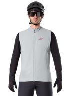 Chaleco Térmico Alpinestars A-Dura, chaleco de ciclismo, gris titanio, usado con un jersey negro de manga larga y casco de ciclismo negro, logo de estrella Alpinestars rojo en el pecho, ligero y con aislamiento para ciclismo de montaña