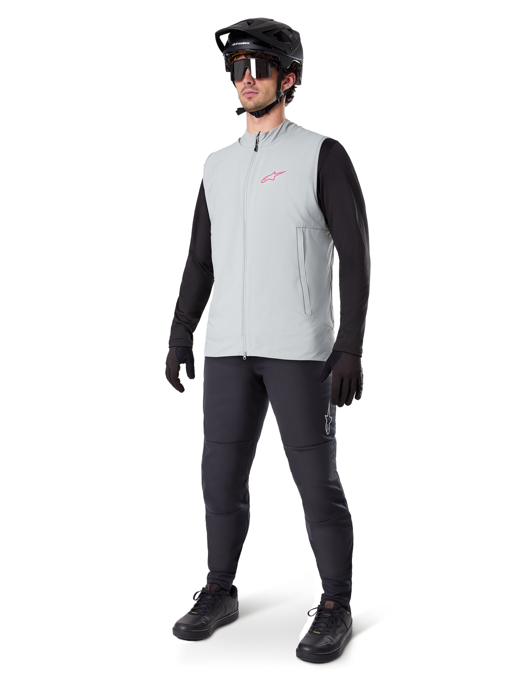 Alpinestars A-Dura Thermal Vest, chaleco de ciclismo gris titanio con logotipo rosa, usado por un modelo con camiseta de manga larga negra, pantalones gris oscuro y casco de bicicleta de montaña negro, equipamiento de alto rendimiento para rodar en climas fríos