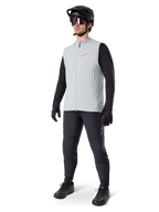 Alpinestars A-Dura Thermal Vest, chaleco de ciclismo gris titanio con logotipo rosa, usado por un modelo con camiseta de manga larga negra, pantalones gris oscuro y casco de bicicleta de montaña negro, equipamiento de alto rendimiento para rodar en climas fríos