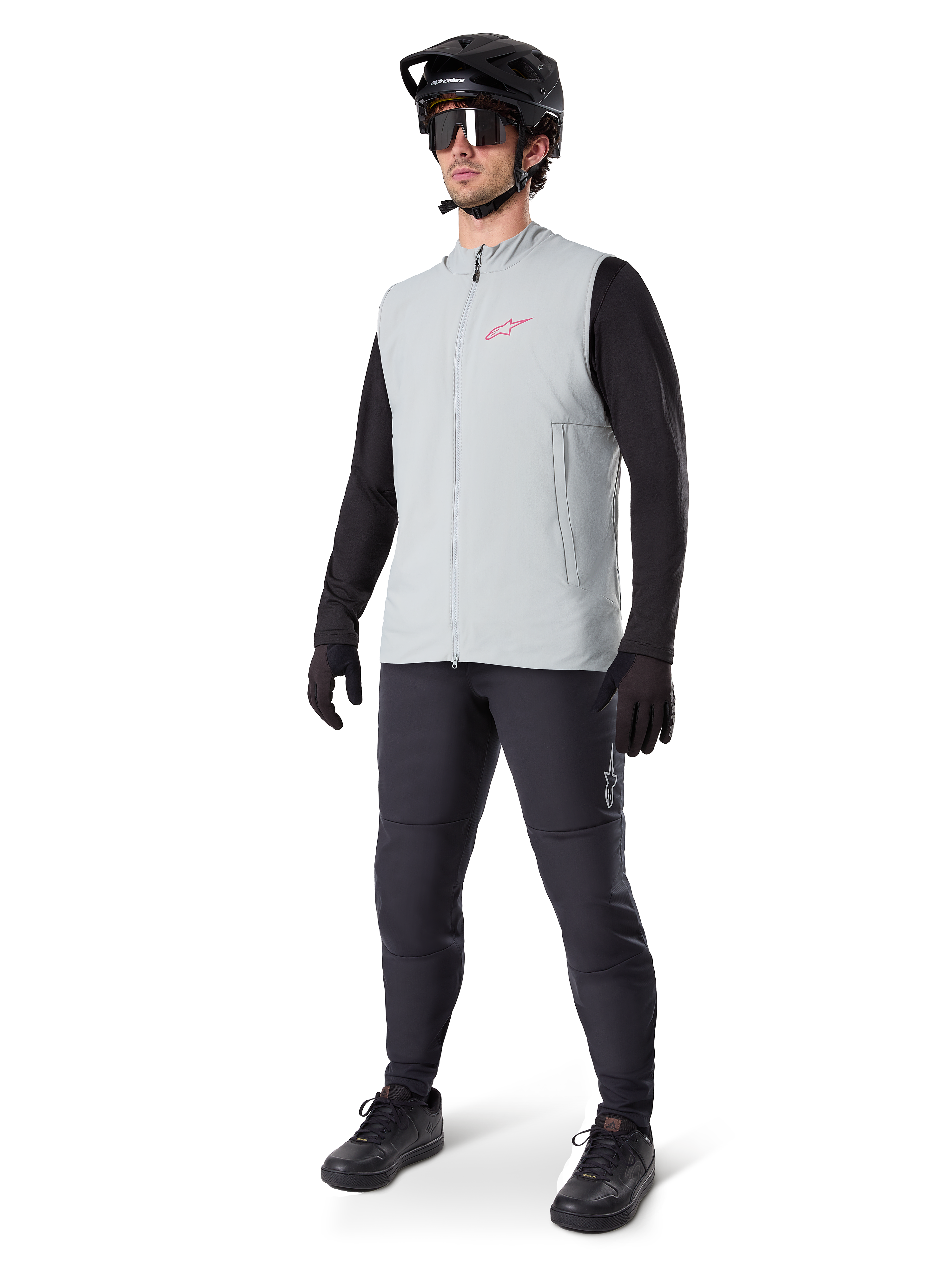 Alpinestars A-Dura Thermal Vest, chaleco de ciclismo gris titanio con logotipo rosa, usado por un modelo con camiseta de manga larga negra, pantalones gris oscuro y casco de bicicleta de montaña negro, equipamiento de alto rendimiento para rodar en climas fríos