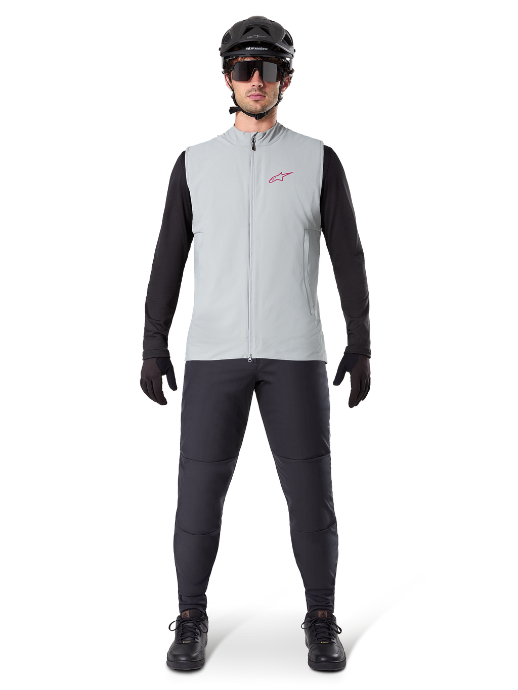 Chaleco térmico Alpinestars A-Dura, chaleco de ciclismo, Gris Titanio, combinado con jersey negro de manga larga y pantalones negros, casco y gafas de sol negros, con logotipo de Alpinestars en rojo, aislamiento térmico ligero para ciclismo de montaña