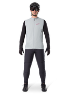 Chaleco térmico Alpinestars A-Dura, chaleco de ciclismo, Gris Titanio, combinado con jersey negro de manga larga y pantalones negros, casco y gafas de sol negros, con logotipo de Alpinestars en rojo, aislamiento térmico ligero para ciclismo de montaña