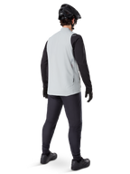 Chaleco térmico Alpinestars A-Dura, Gris Titanium, vista posterior del modelo que lleva el chaleco de ciclismo con aislamiento sobre una prenda negra de manga larga y pantalones oscuros, completado con casco de bicicleta de montaña y guantes negros, diseñado para el ciclismo todoterreno en climas fríos