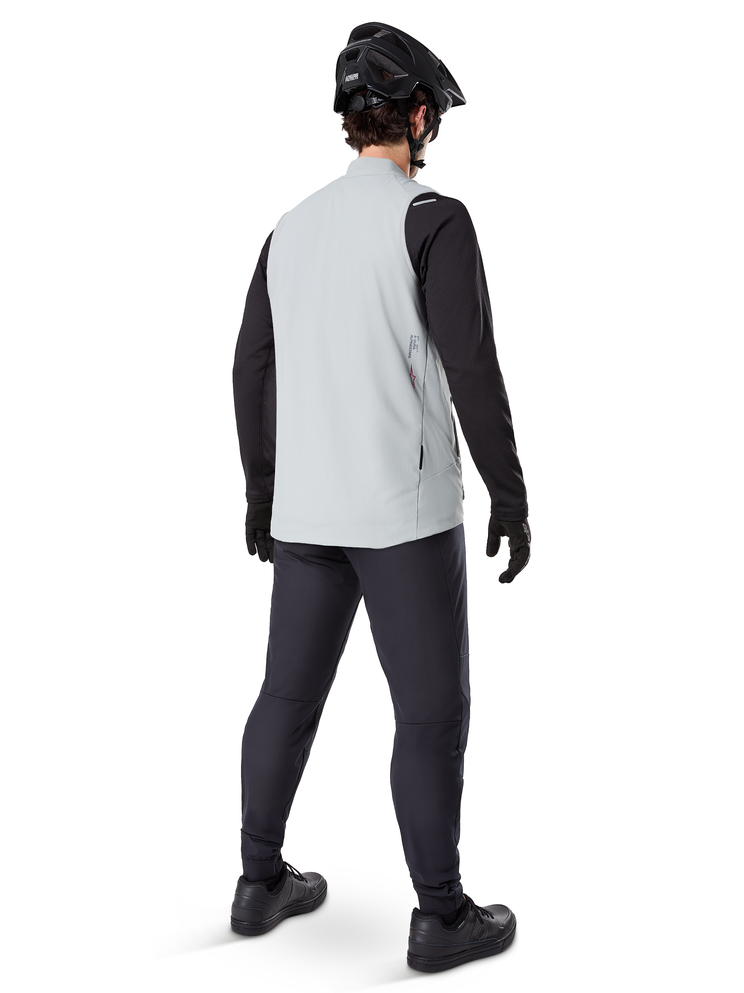 Chaleco térmico Alpinestars A-Dura, Gris Titanium, vista posterior del modelo que lleva el chaleco de ciclismo con aislamiento sobre una prenda negra de manga larga y pantalones oscuros, completado con casco de bicicleta de montaña y guantes negros, diseñado para el ciclismo todoterreno en climas fríos