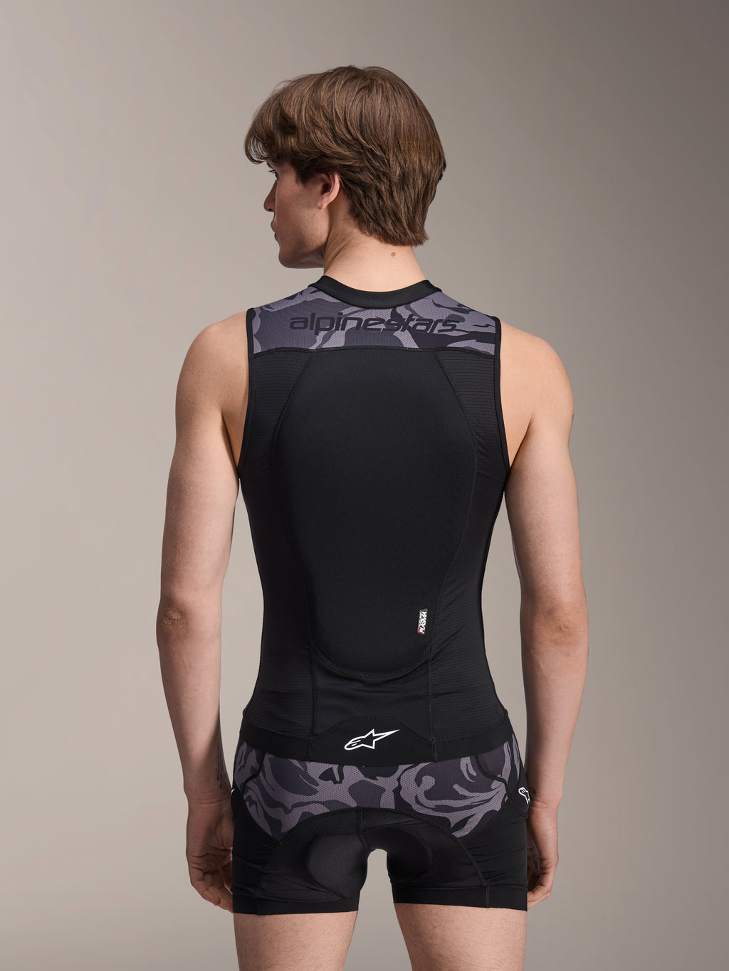 Chaleco de protección Alpinestars A-Motion Plasma, Black Camo, vista trasera en modelo masculino, con construcción de malla transpirable, protector de espalda Nucleon Plasma integrado, detalles de camuflaje gris en los hombros y la cintura, y logotipo de Alpinestars.