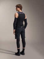 Modelo masculino de espaldas vistiendo el Chaleco de Protección Alpinestars A-Motion Plasma, Black Camo, diseño de malla sin mangas con protector de espalda integrado, patrón de camuflaje gris en los hombros, usado con coderas negras y pantalones cortos de ciclismo de montaña, equipamiento de ciclismo profesional