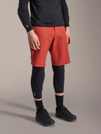 Rodillera Alpinestars A-Motion Plasma, protector de rodilla para MTB, negro, usado con pantalones cortos rojos y zapatillas de ciclismo de montaña negras, diseño de perfil bajo tipo manga con almohadillas protectoras contorneadas y malla transpirable.