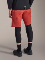 Alpinestars A-Motion Plasma Knee Sleeve, rodillera de MTB negra, usada con pantalones cortos de ciclismo de montaña rojos y zapatillas de ciclismo negras, vista trasera que muestra el diseño de perfil bajo y fácil de poner para ciclismo de montaña