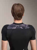 Chaqueta protectora Alpinestars A-Motion Plasma de manga corta, vista trasera de la parte superior del torso, negra con panel de camuflaje gris en los hombros con logotipo de Alpinestars, tejido de malla elástica transpirable para protección de MTB