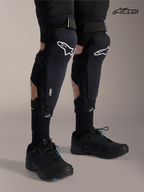 Alpinestars A-Impact Plasma Pro, protectores de rodilla y espinilla para bicicleta de montaña, negros con logotipo blanco, vista frontal en modelo con sistema de triple correa y protección Nucleon Plasma