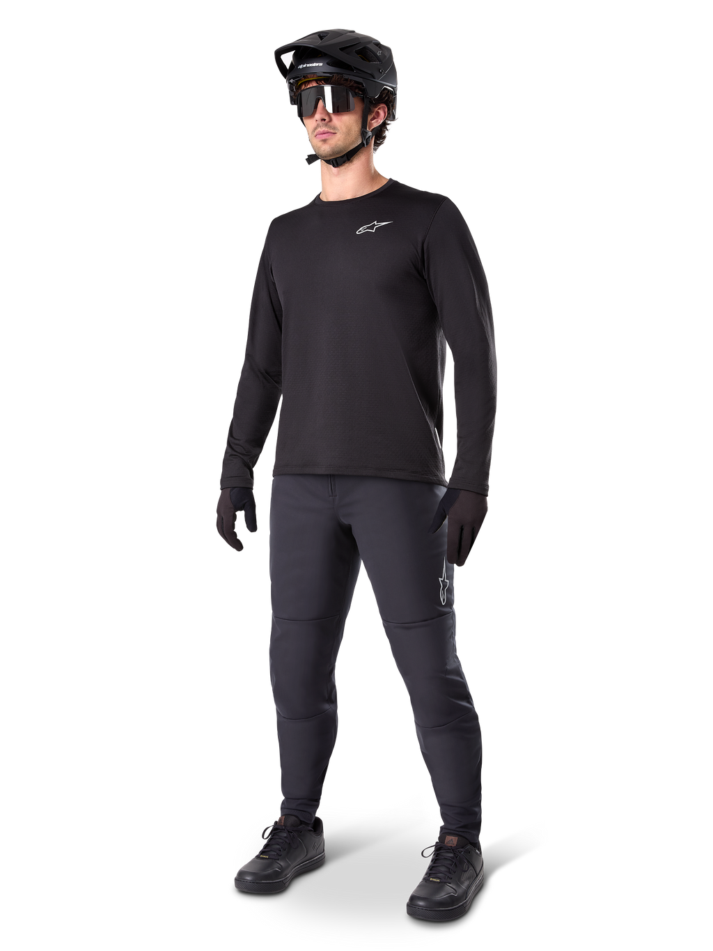 Ciclista de montaña vistiendo los Pantalones Térmicos A-Dura de Alpinestars en color negro, combinados con un jersey negro de manga larga, casco negro y gafas de sol, con el logotipo plateado de Alpinestars en el muslo izquierdo, diseñados para recorrer senderos en climas fríos.