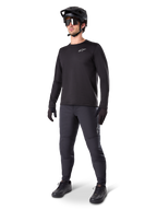 Ciclista de montaña vistiendo los Pantalones Térmicos A-Dura de Alpinestars en color negro, combinados con un jersey negro de manga larga, casco negro y gafas de sol, con el logotipo plateado de Alpinestars en el muslo izquierdo, diseñados para recorrer senderos en climas fríos.